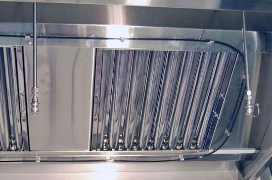 Wet chemical fire suppression nozzles installed inside a stainless steel commercial kitchen extract canopy